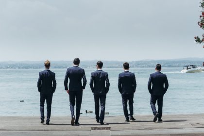 Five men in classy suits walk towards the blue sea