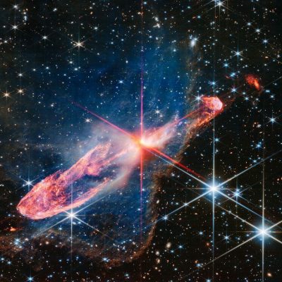 The NASA/ESA/CSA James Webb Space Telescope has captured a high-resolution image of a tightly bound pair of actively forming stars, known as Herbig-Haro 46/47, in near-infrared light. Look for them at the centre of the red diffraction spikes. The stars are buried deeply, appearing as an orange-white splotch. They are surrounded by a disc of gas and dust that continues to add to their mass. Herbig-Haro 46/47 is an important object to study because it is relatively young — only a few thousand years old. Stars take millions of years to form. Targets like this also give researchers insight into how stars gather mass over time, potentially allowing them to model how our own Sun, a low-mass star, formed. The two-sided orange lobes were created by earlier ejections from these stars. The stars’ more recent ejections appear as blue, thread-like features, running along the angled diffraction spike that covers the orange lobes. Actively forming stars ingest the gas and dust that immediately surrounds them in a disc (imagine an edge-on circle encasing them). When the stars ‘eat’ too much material in too short a time, they respond by sending out two-sided jets along the opposite axis, settling down the star’s spin, and removing mass from the area. Over millennia, these ejections regulate how much mass the stars retain. Don’t miss the delicate, semi-transparent blue cloud. This is a region of dense dust and gas, known as a nebula. Webb’s crisp near-infrared image lets us see through its gauzy layers, showing off a lot more of Herbig-Haro 46/47, while also revealing a wide range of stars and galaxies that lie far beyond it. The nebula’s edges transform into a soft orange outline, like a backward L along the right and bottom of the image. The blue nebula influences the shapes of the orange jets shot out by the central stars. As ejected material rams into the nebula on the lower left, it takes on wider shapes, because there is more opportunity for the jets to interac