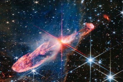 The NASA/ESA/CSA James Webb Space Telescope has captured a high-resolution image of a tightly bound pair of actively forming stars, known as Herbig-Haro 46/47, in near-infrared light. Look for them at the centre of the red diffraction spikes. The stars are buried deeply, appearing as an orange-white splotch. They are surrounded by a disc of gas and dust that continues to add to their mass. Herbig-Haro 46/47 is an important object to study because it is relatively young — only a few thousand years old. Stars take millions of years to form. Targets like this also give researchers insight into how stars gather mass over time, potentially allowing them to model how our own Sun, a low-mass star, formed. The two-sided orange lobes were created by earlier ejections from these stars. The stars’ more recent ejections appear as blue, thread-like features, running along the angled diffraction spike that covers the orange lobes. Actively forming stars ingest the gas and dust that immediately surrounds them in a disc (imagine an edge-on circle encasing them). When the stars ‘eat’ too much material in too short a time, they respond by sending out two-sided jets along the opposite axis, settling down the star’s spin, and removing mass from the area. Over millennia, these ejections regulate how much mass the stars retain. Don’t miss the delicate, semi-transparent blue cloud. This is a region of dense dust and gas, known as a nebula. Webb’s crisp near-infrared image lets us see through its gauzy layers, showing off a lot more of Herbig-Haro 46/47, while also revealing a wide range of stars and galaxies that lie far beyond it. The nebula’s edges transform into a soft orange outline, like a backward L along the right and bottom of the image. The blue nebula influences the shapes of the orange jets shot out by the central stars. As ejected material rams into the nebula on the lower left, it takes on wider shapes, because there is more opportunity for the jets to interac